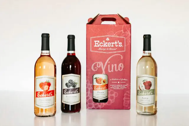 Three bottles of Eckert's fruit wine flank a boxed Eckert's Vino product on a plain surface against a white backdrop.
