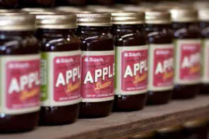 Rows of jars labeled "Apple Butter" are lined up on a wooden shelf, with a focus on one jar in the center.