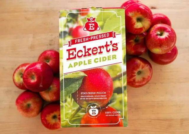 Sweet Apple Cider in liter container displayed on wooden table with apples.