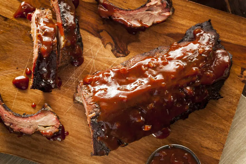 Applewood Smoked Ribs - cooked and sauced bbq ribs cut on wooden cutting board