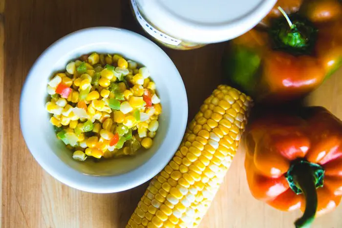Eckert's Corn O'Brien in white bowl displayed with corn on the cob and red peppers.
