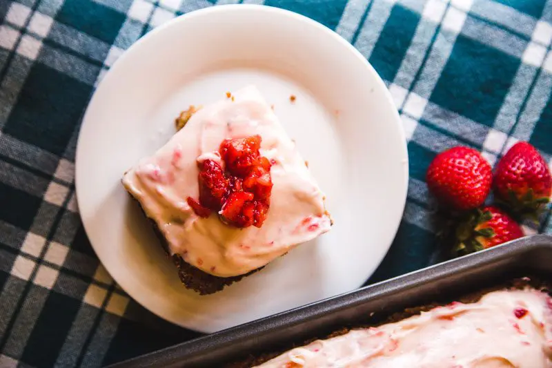 A Slice of Strawberry Cake with Strawberry Cream Cheese Frosting on a whie plate with black and white table linen.