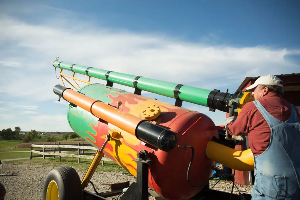 A person operates a colorful, large cannon-style device likely used for launching items for entertainment.