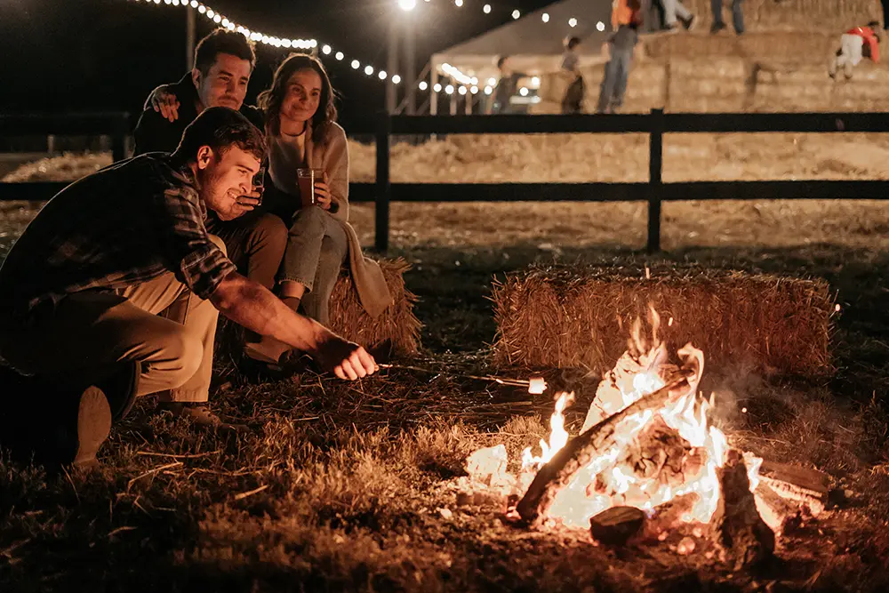 3 individuals sitting on hay bales roasting marshmallows in Millstadt for bonfire nights