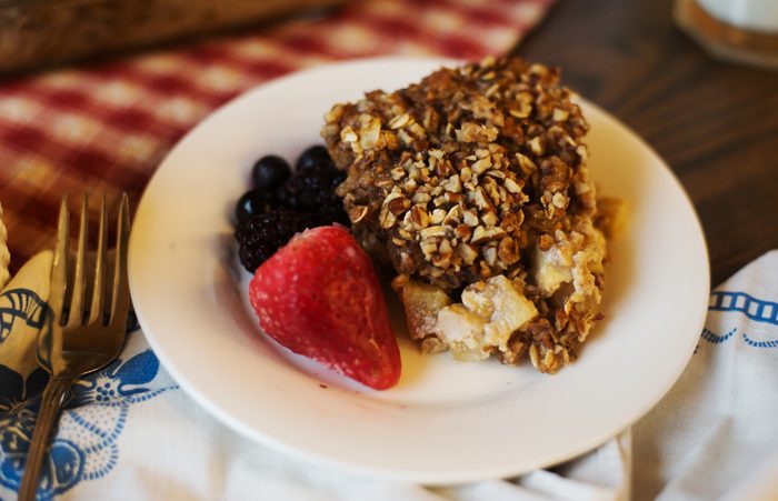 A plate with a nut-crusted pastry and fresh berries on a table with a patterned cloth.