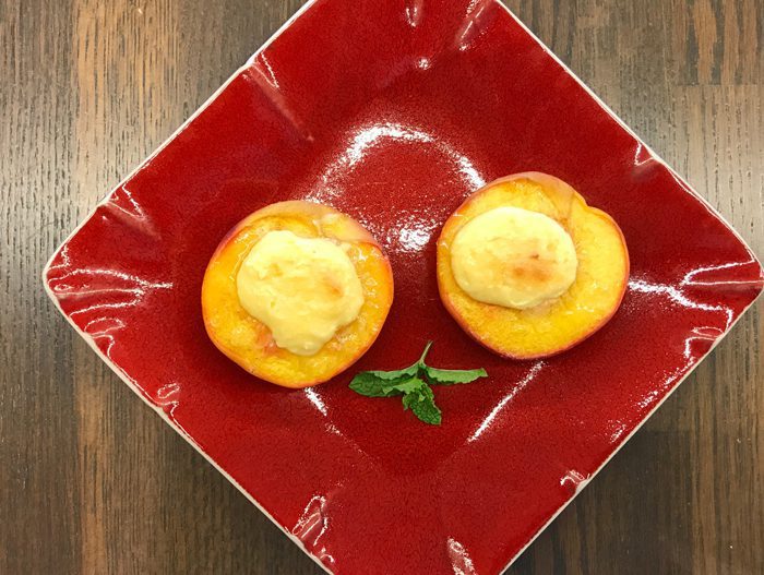 Two lemon tarts with a dollop of meringue on top are served on a red square plate with a green leaf garnish.