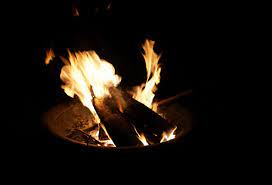 A bright campfire burns in the darkness with fiery orange flames and dark background.