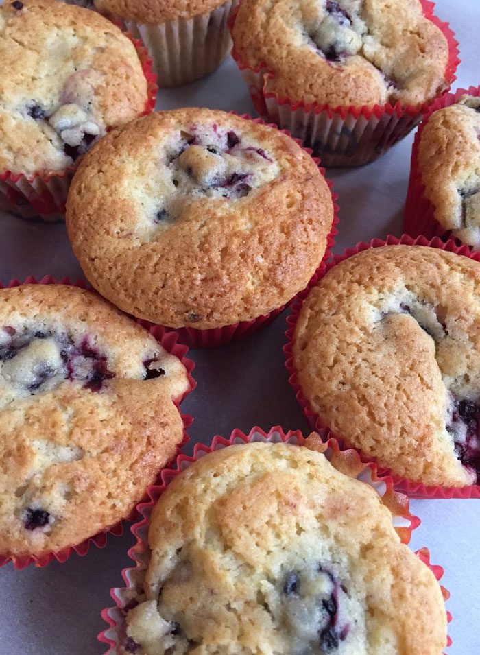 Freshly baked muffins with berries are arranged on a surface, displaying their golden-brown tops and fruit-filled insides.