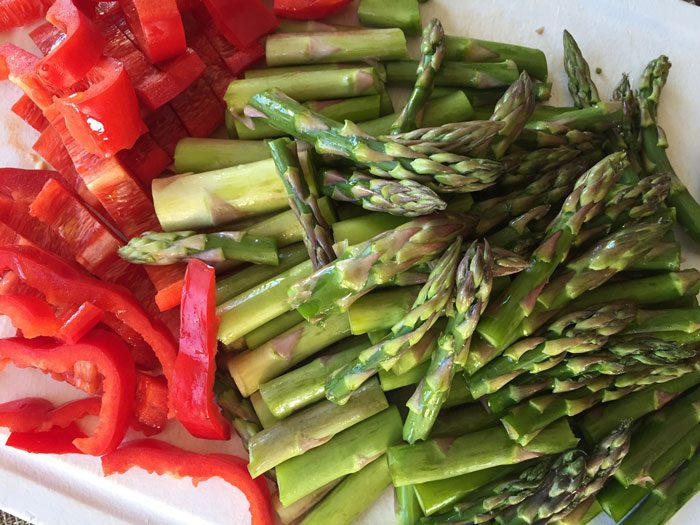 Freshly chopped red bell peppers and asparagus spears are arranged on a white plate.