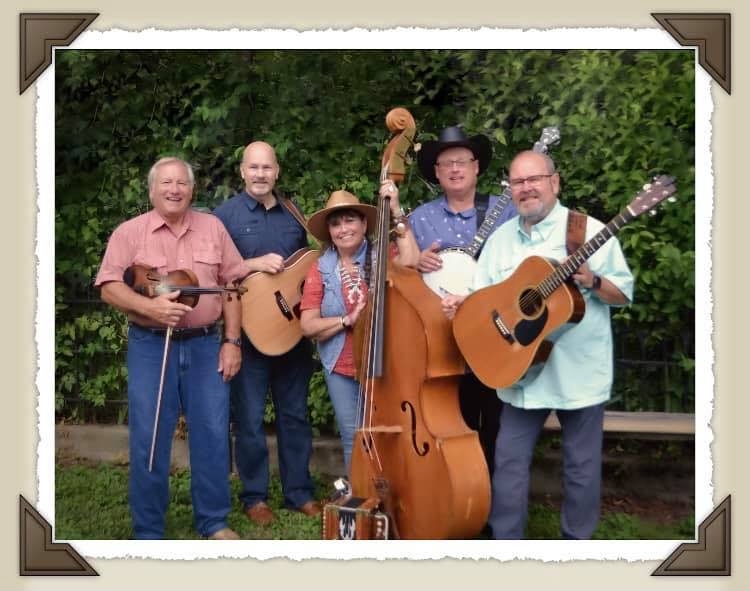 A group of musicians with string instruments poses outdoors.